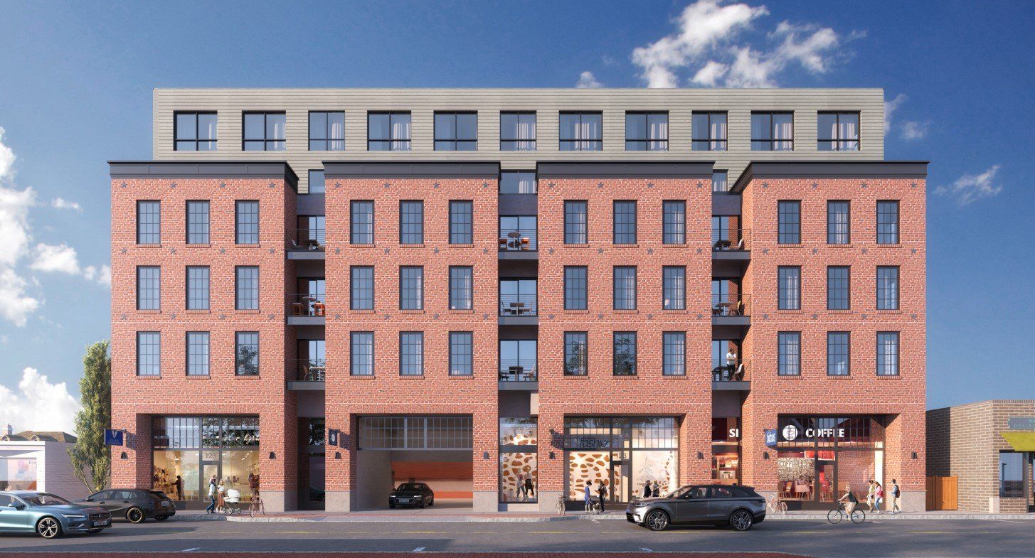A multi-story brick apartment building with ground-floor storefronts and a recessed parking entrance, under a blue sky.