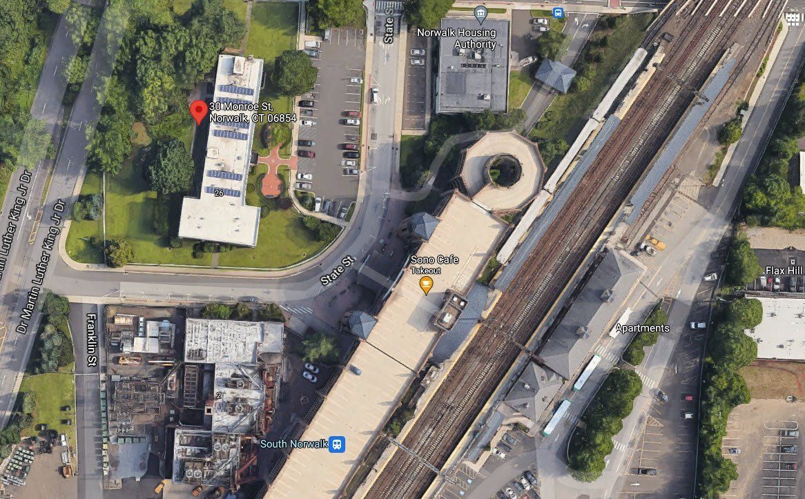 Aerial view of a parking garage near a train track, a nearby office building, and access roads.