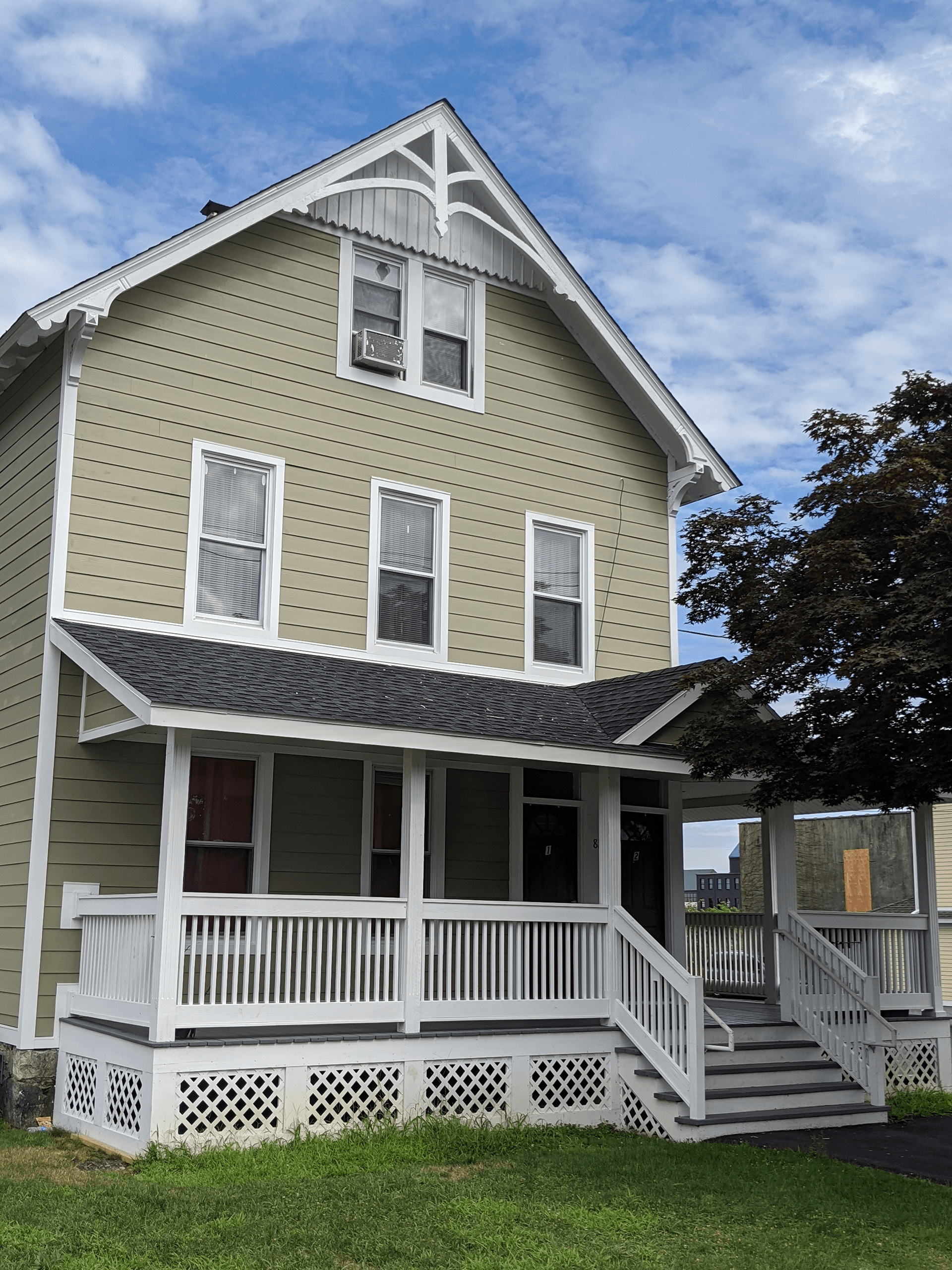 A two-story light green Victorian house with a white wrap-around porch, lattice skirting, and decorative wood trim.
