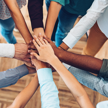 A group of people placing their hands on top of each other in a circle, symbolizing unity and teamwork.