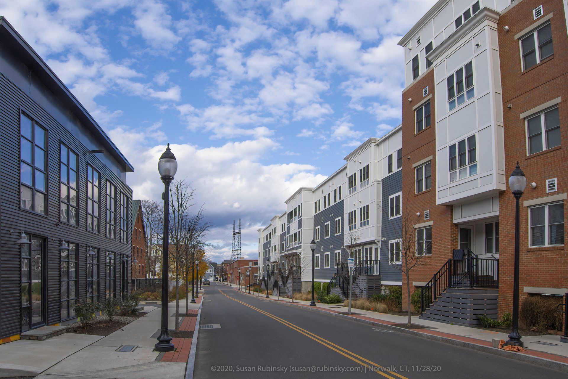 A street scene showing a modern apartment complex on the right and a dark, multi-windowed building on the left.
