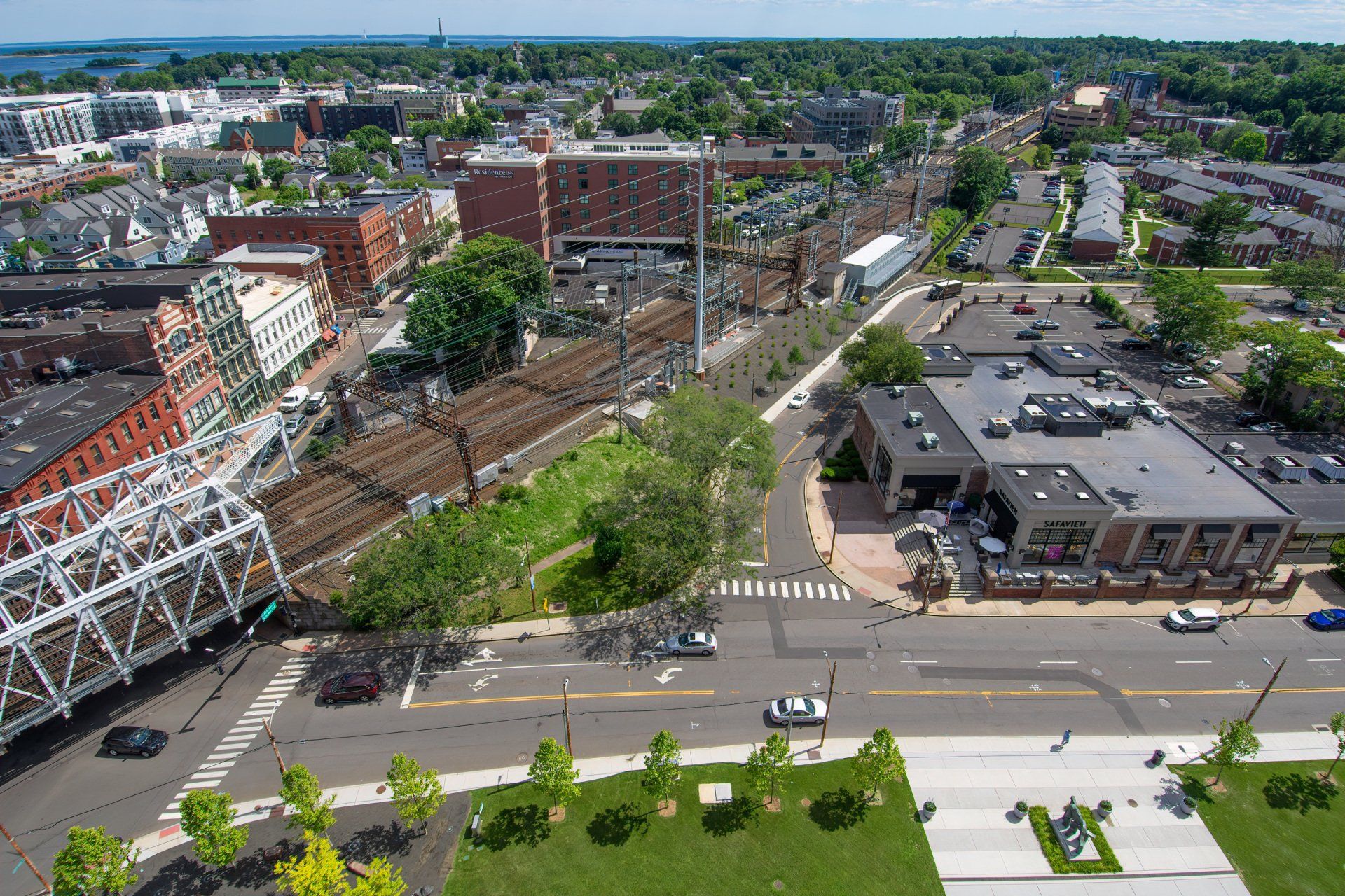 Aerial view of a city street intersection featuring a bridge, railway tracks, surrounding buildings, and green spaces.