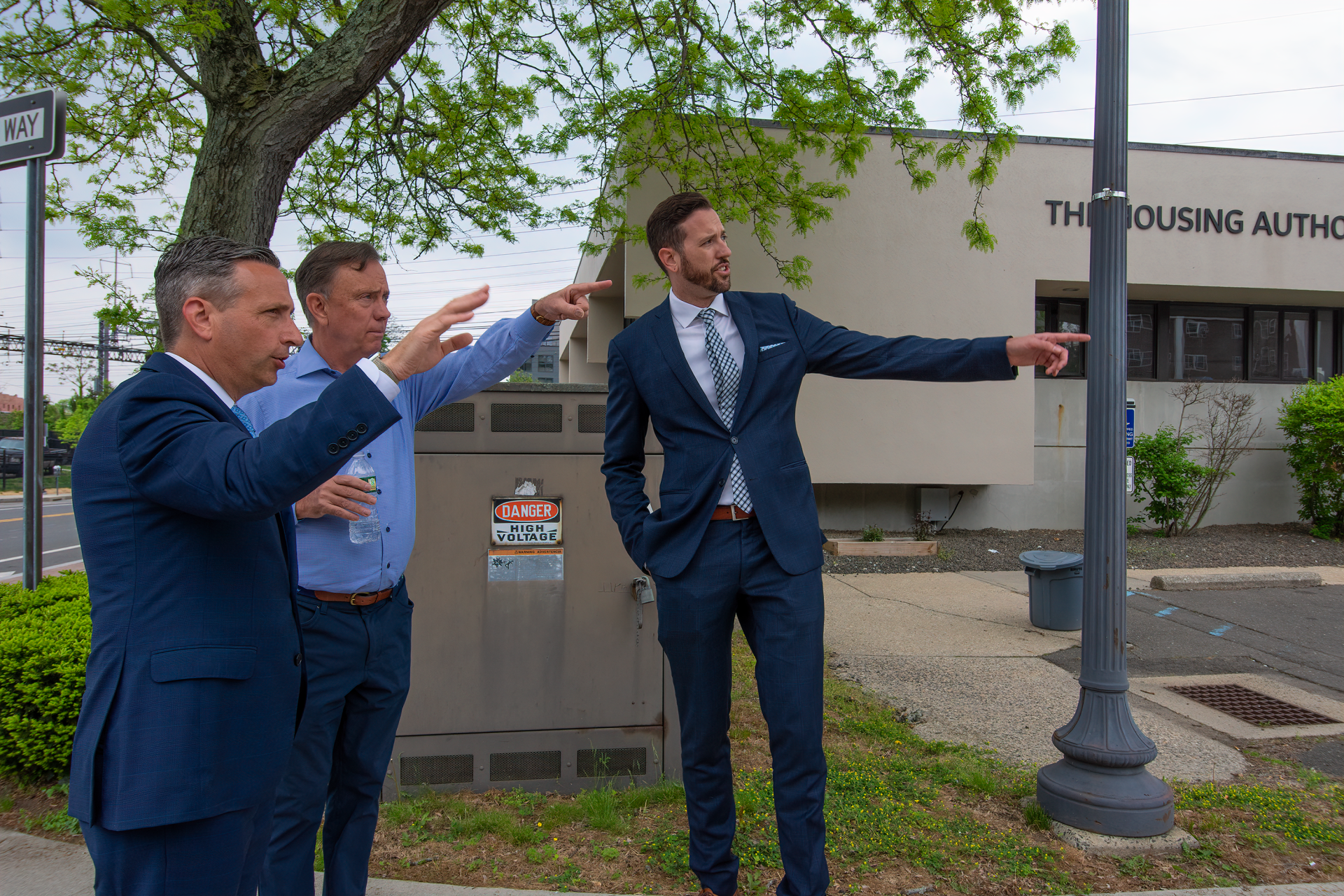 Three professionals in suits point toward a building labeled