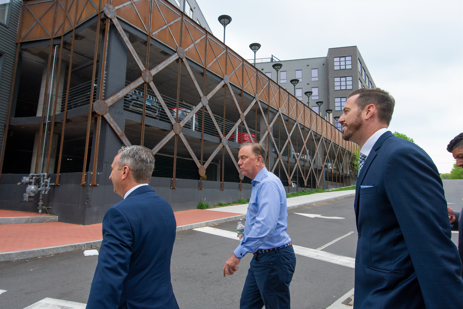 Three professionals in business attire walk past a modern building featuring a decorative, X-patterned metal facade.