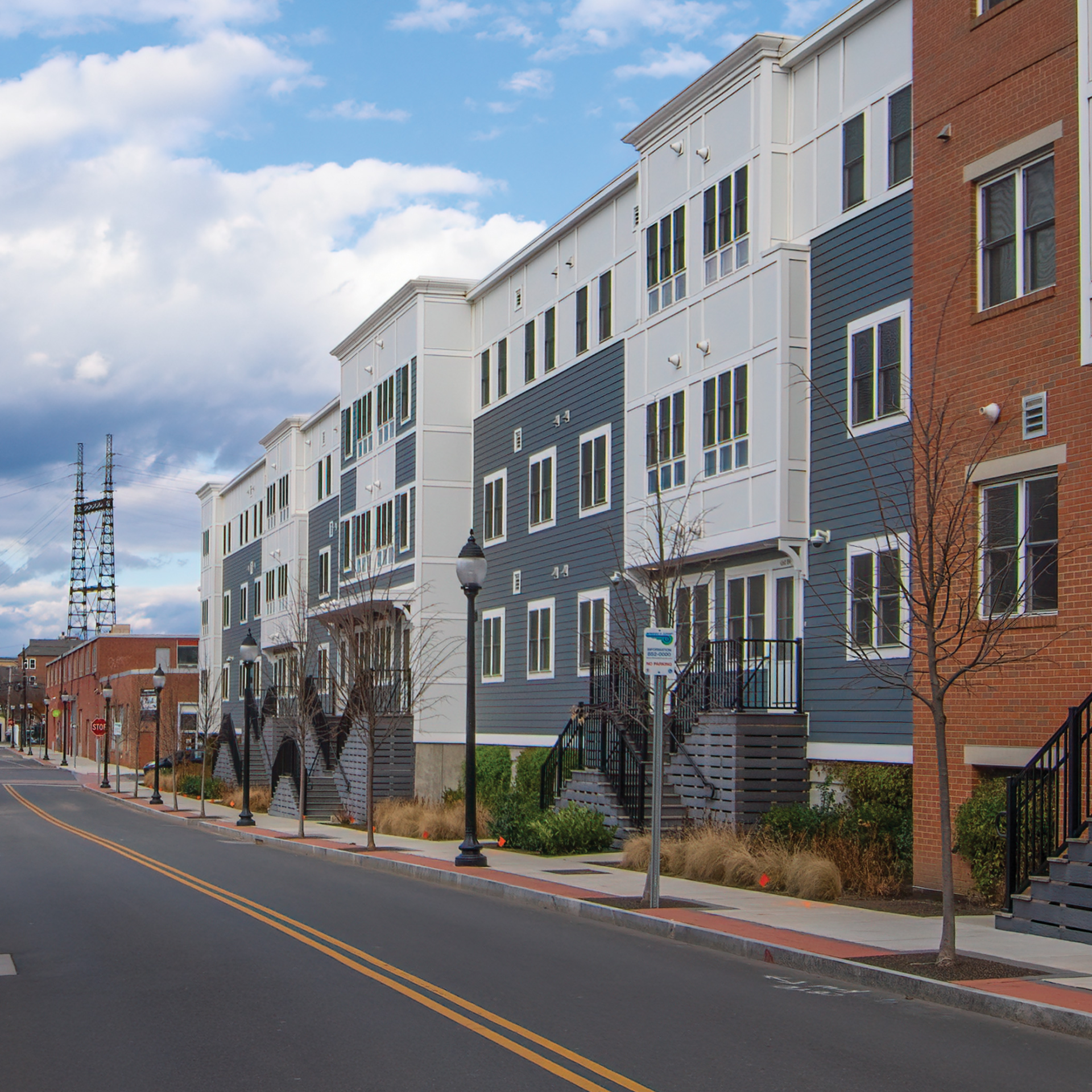 A multi-story building with white, blue, and brick facade elements lines a paved street under a cloudy sky.