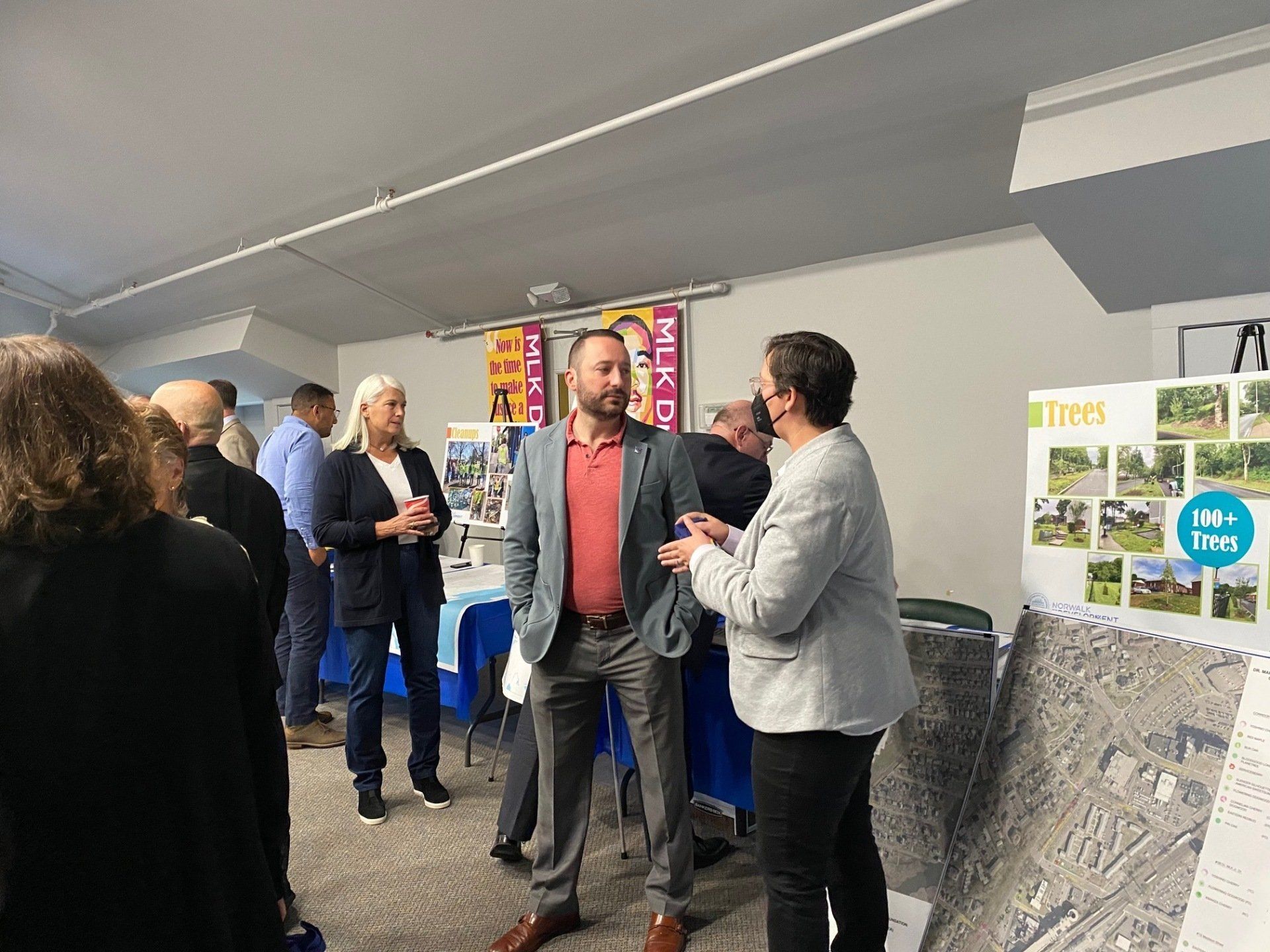 People in a room talk near display boards during an indoor community meeting or presentation.