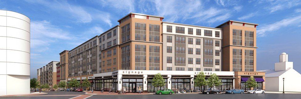 A multi-story building featuring modern residential apartments above ground-floor retail shops under a bright blue sky.