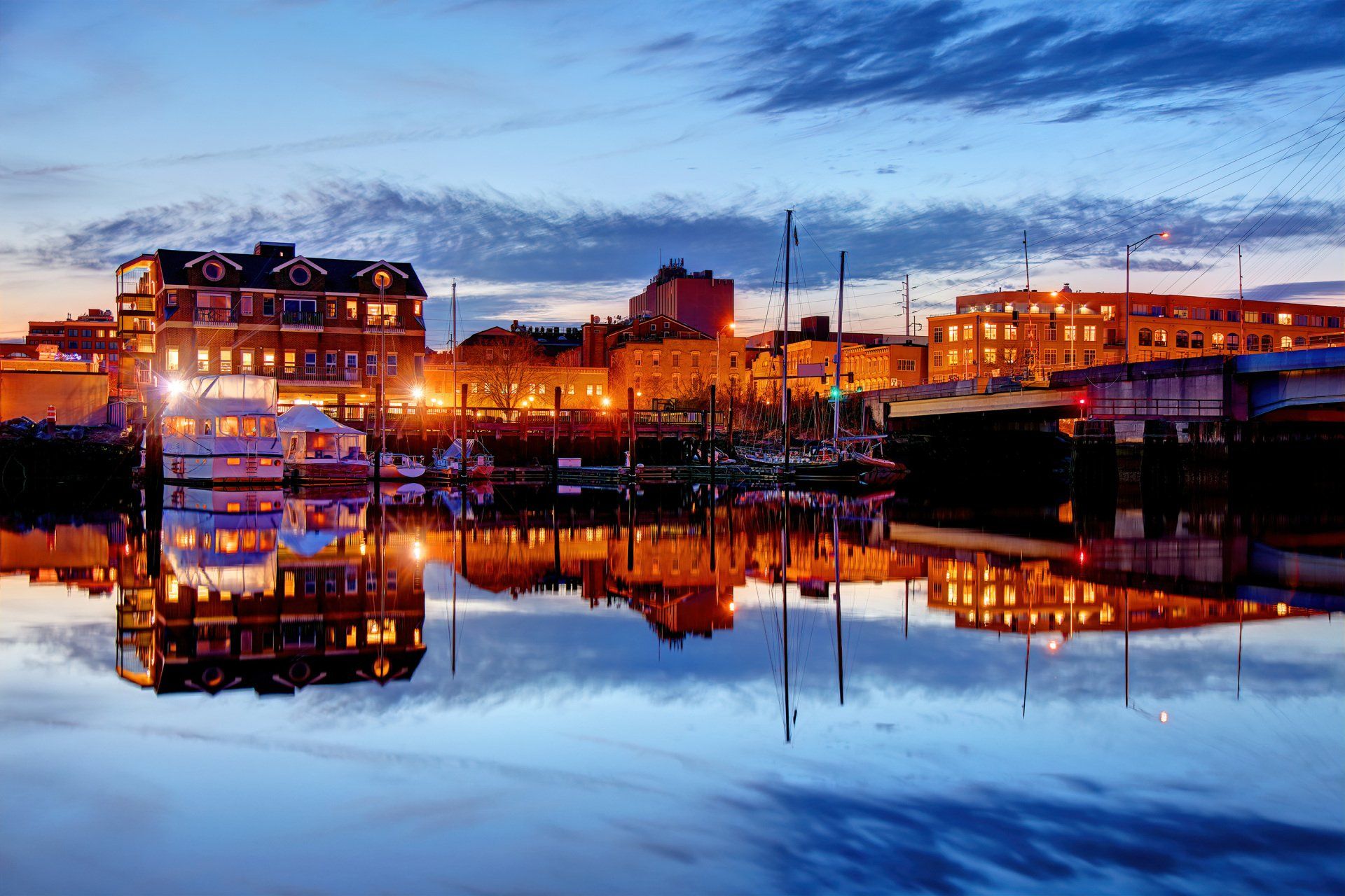 Buildings at a waterfront reflecting in calm water during a blue hour twilight.