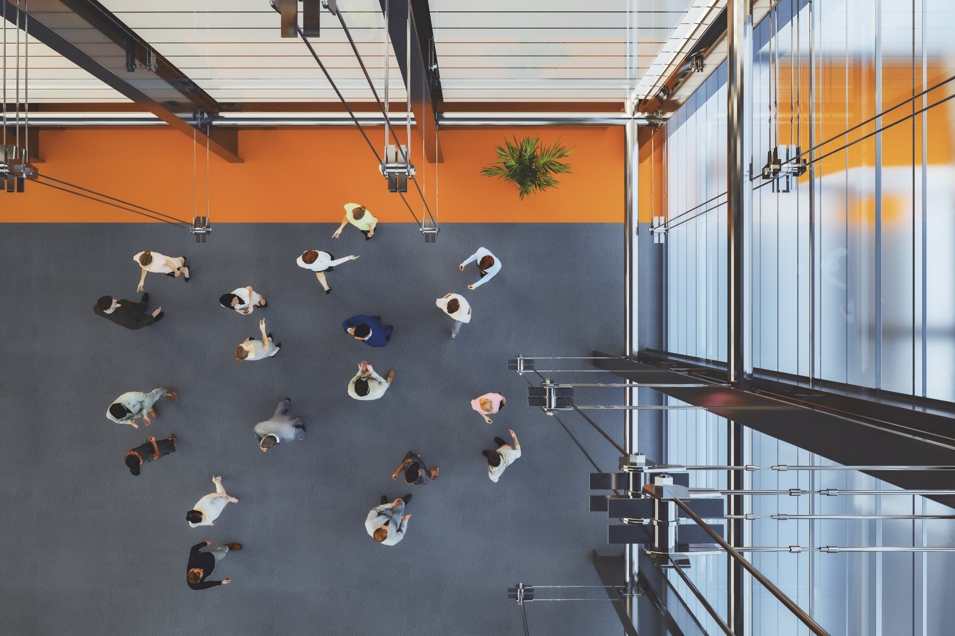 A high-angle view of a diverse group of people walking across a large grey floor in a modern, orange-walled building.