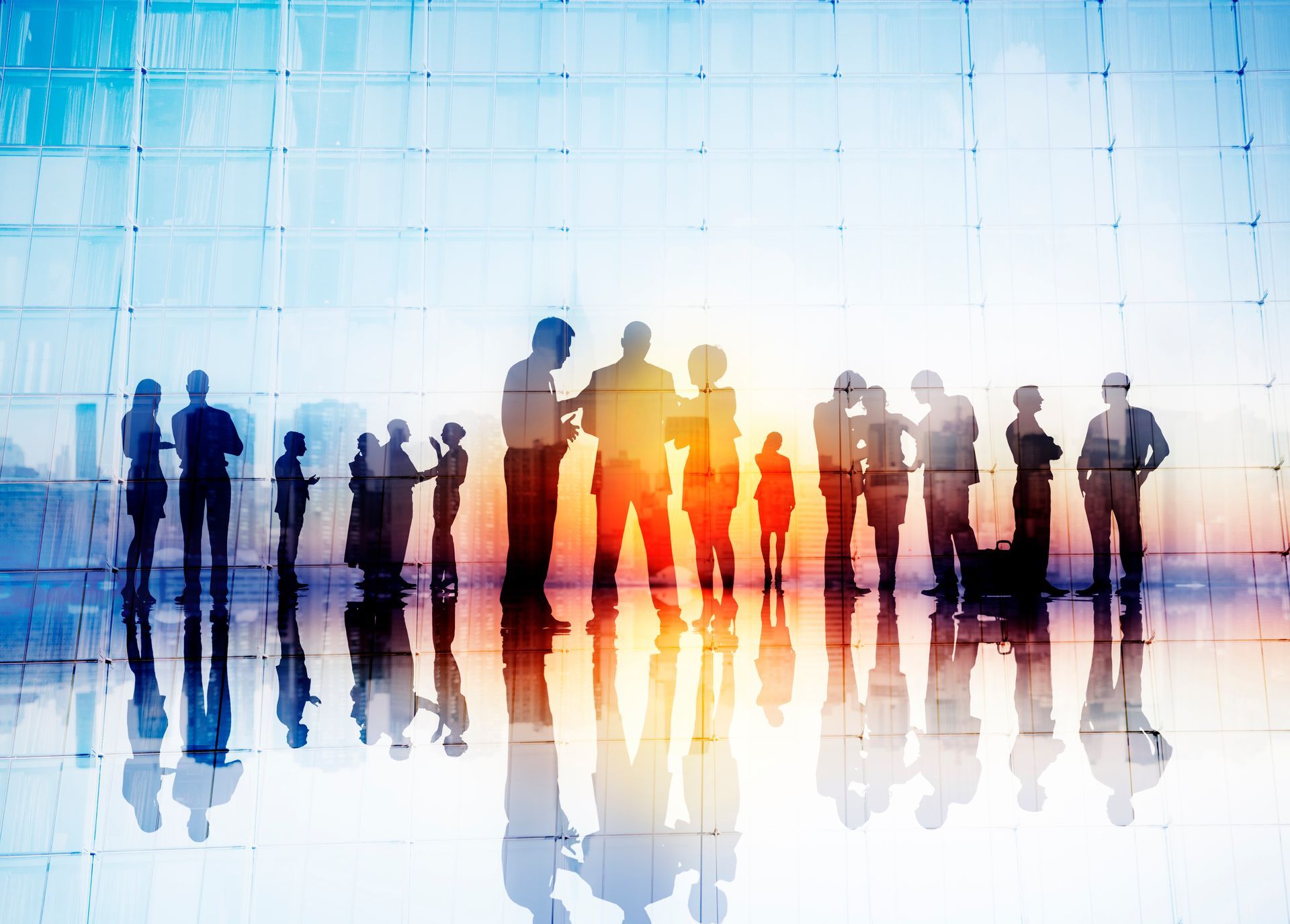 A group of people standing in silhouette against a large, sunlit window, reflecting on a polished floor.