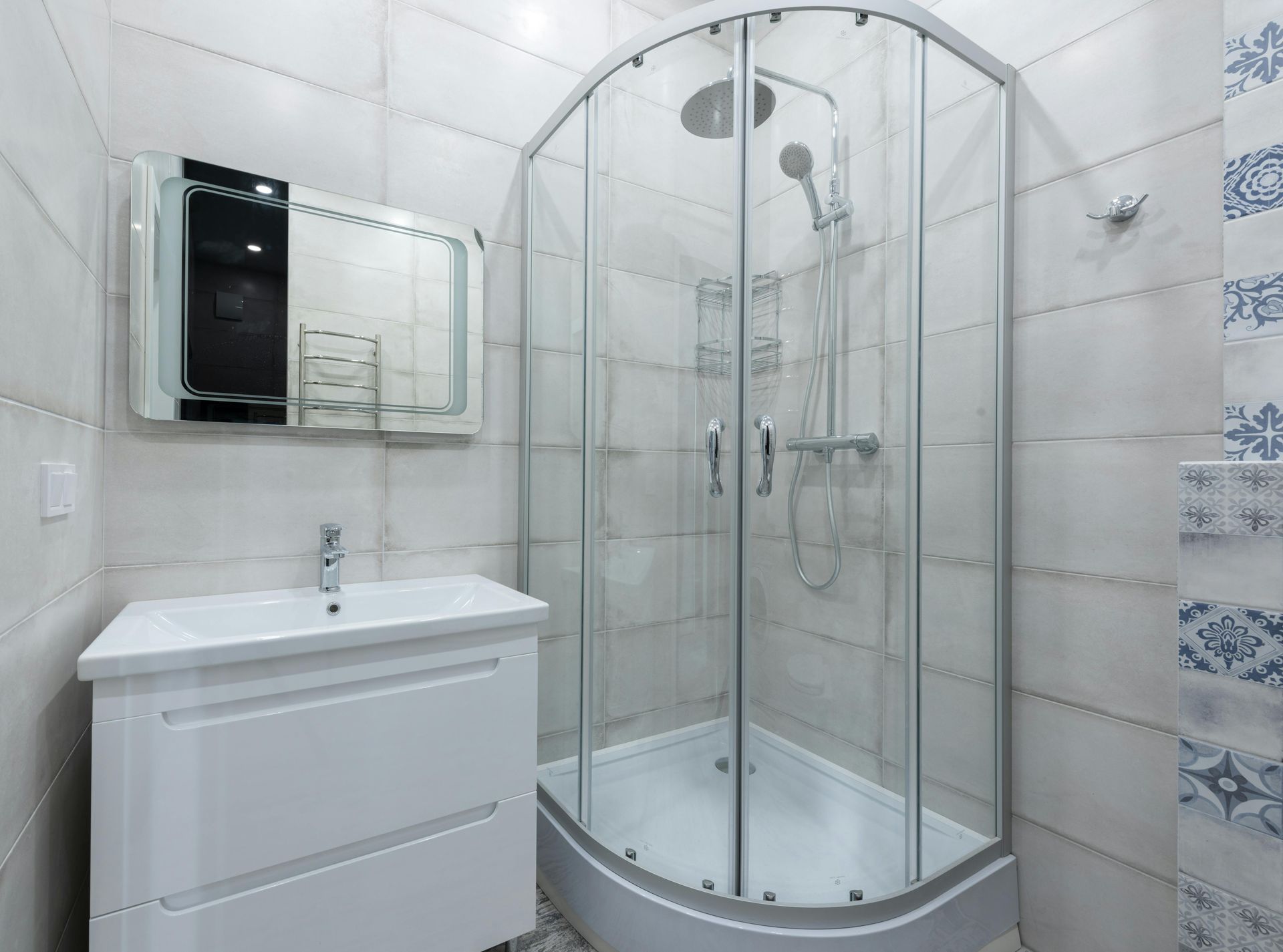 Modern bathroom with curved glass shower, white vanity, and decorative tile accents