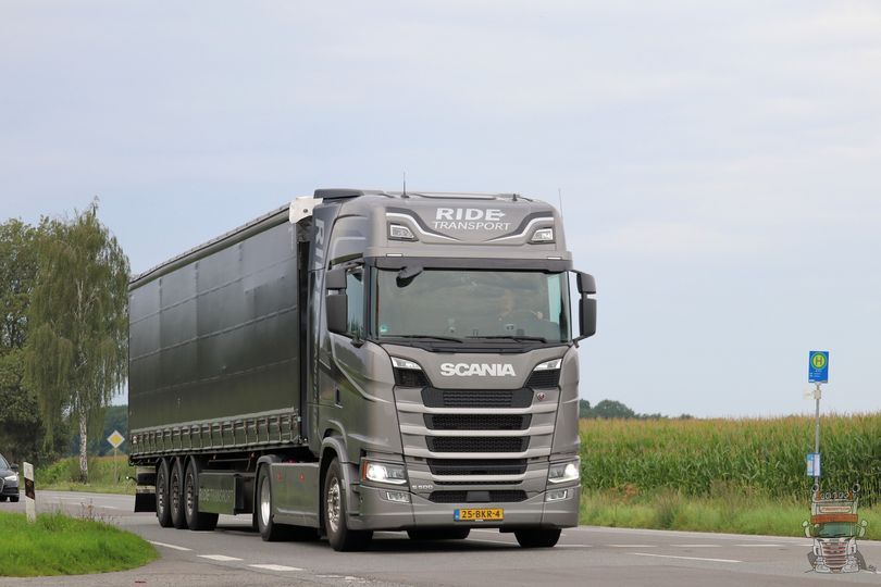 Grijze Scania-vrachtwagen op een weg. De vrachtwagen heeft een oplegger en rijdt in de richting van de kijker.
