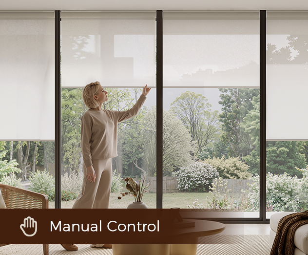 A person adjusting a white window roller shade by hand in a bright, modern room overlooking a garden.