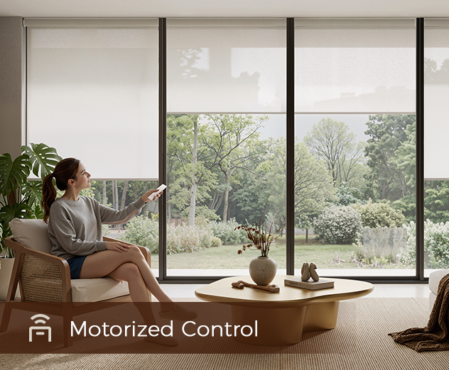A person sits in a chair using a remote to adjust motorized roller shades in a room with a large window and garden view.