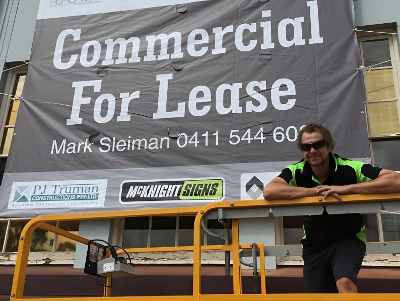 A Man Leaning On A Railing In Front Of A Large Commercial For Lease Sign — McKnight Signs In Hillvue, NSW