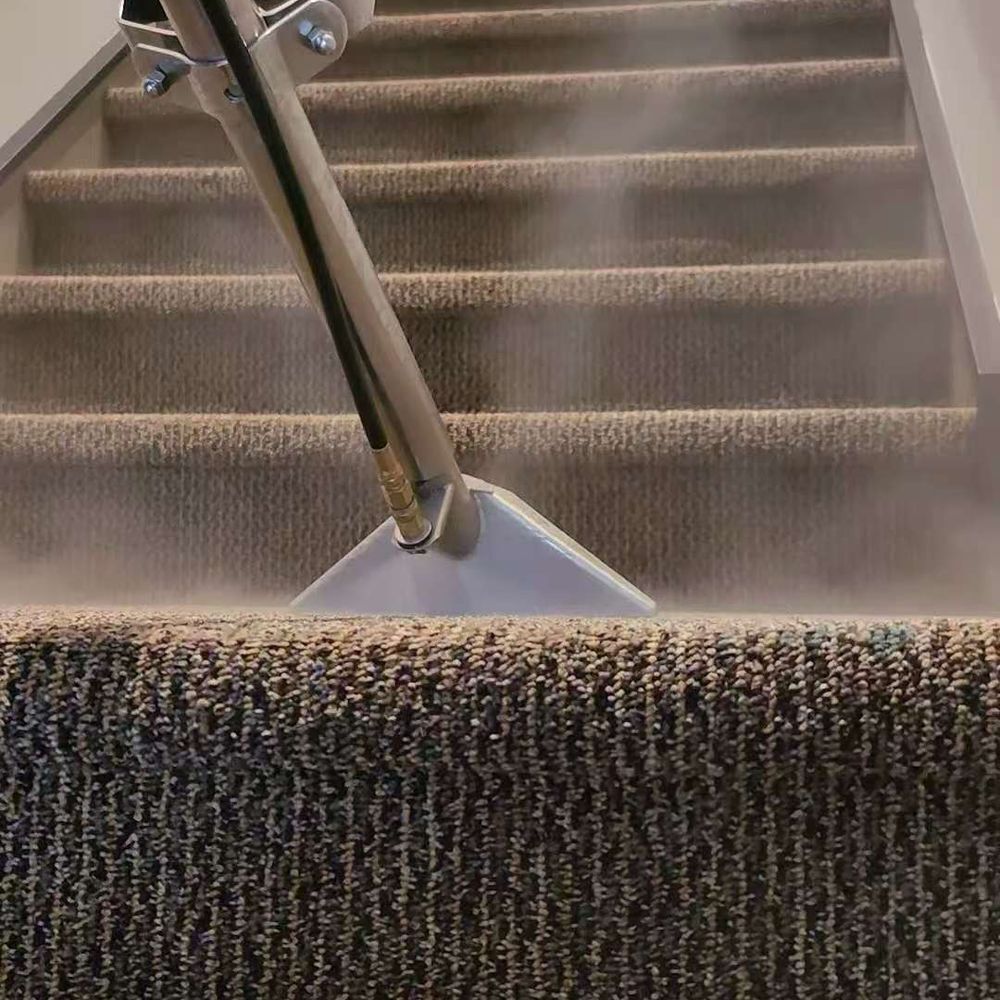 Carpeted stairs being steam cleaned with a cleaning tool, producing visible steam.