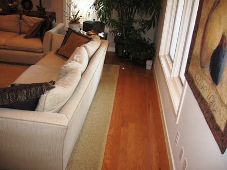 Beige sofa with brown pillows, green rug, hardwood floor, large window, and artwork.