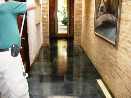 Man with cane in hallway, shiny dark floor, brick walls, art, doorway to outside.