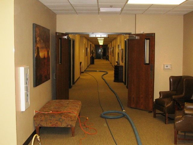 Hallway with open doors, a bench, chairs, and a vacuum hose on carpet.