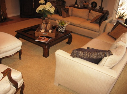 Living room with beige sofas, coffee table with flowers, and two armchairs on beige carpet.