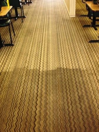 Tan carpet in a room with a visible difference in color from being cleaned. Desks and chairs are in the background.