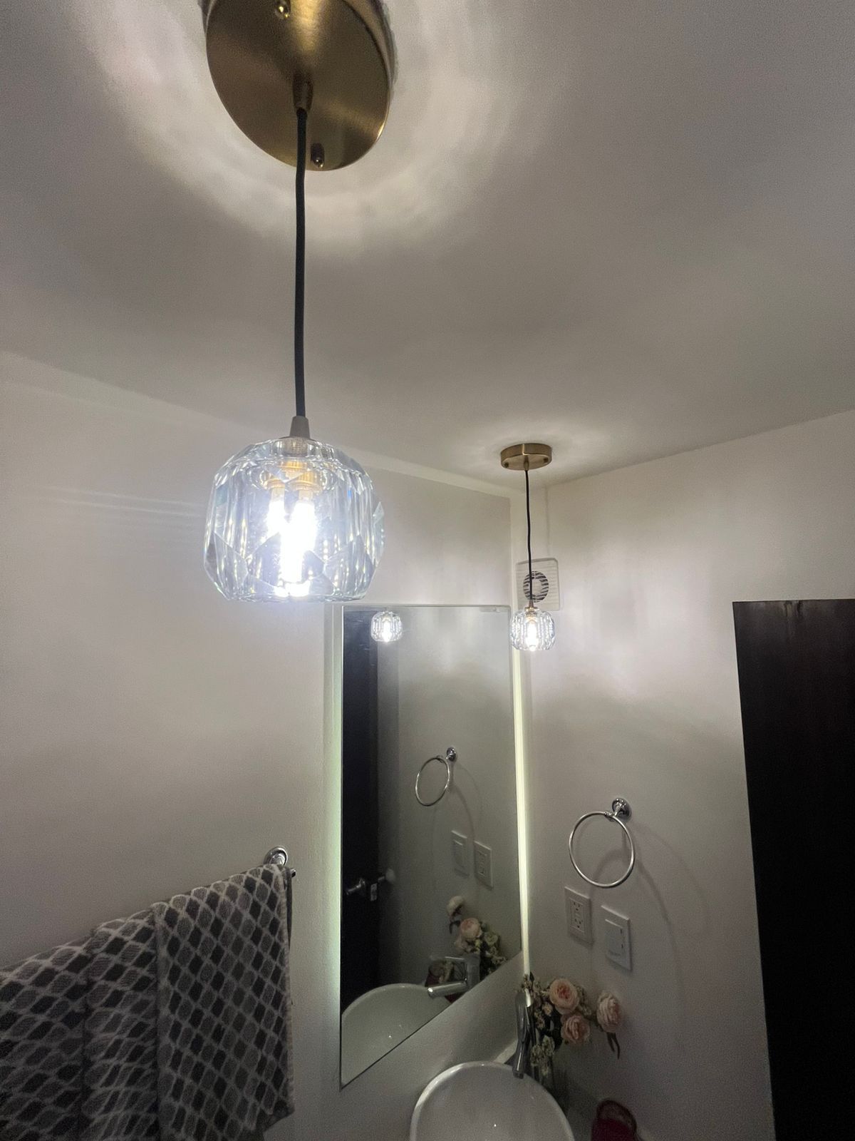 Dos modernas lámparas colgantes de latón cuelgan del techo sobre un espejo de baño, un lavabo y un toallero.