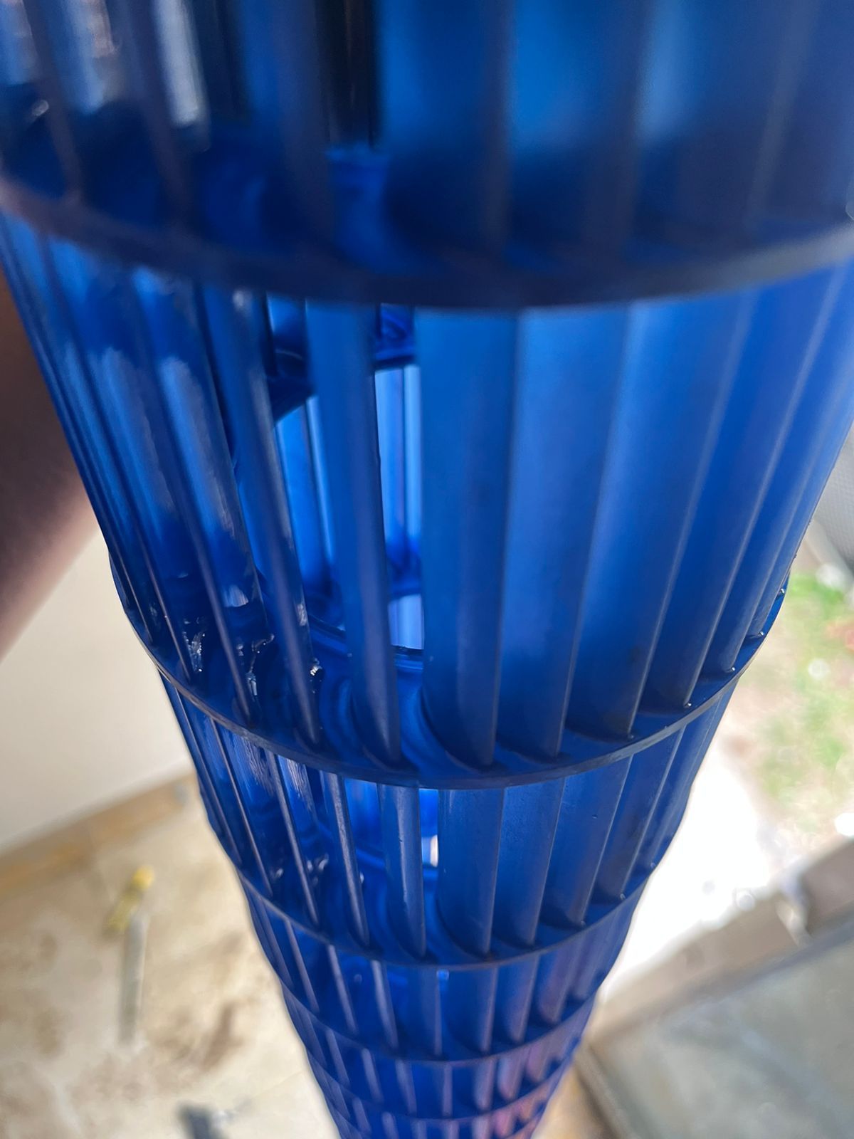 Una rueda de soplador cilíndrica azul de una unidad de aire acondicionado, que muestra sus aspas verticales detalladas y su estructura interior.