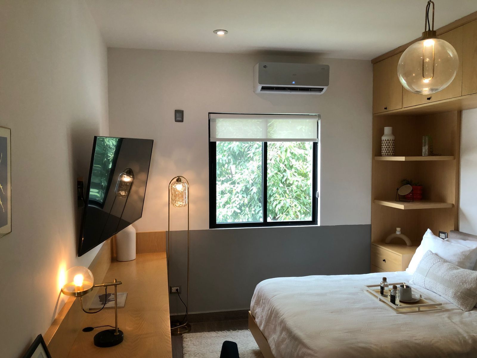 Dormitorio moderno con cama con sábanas blancas, TV de pared, ventana, estantería de madera e iluminación cálida.