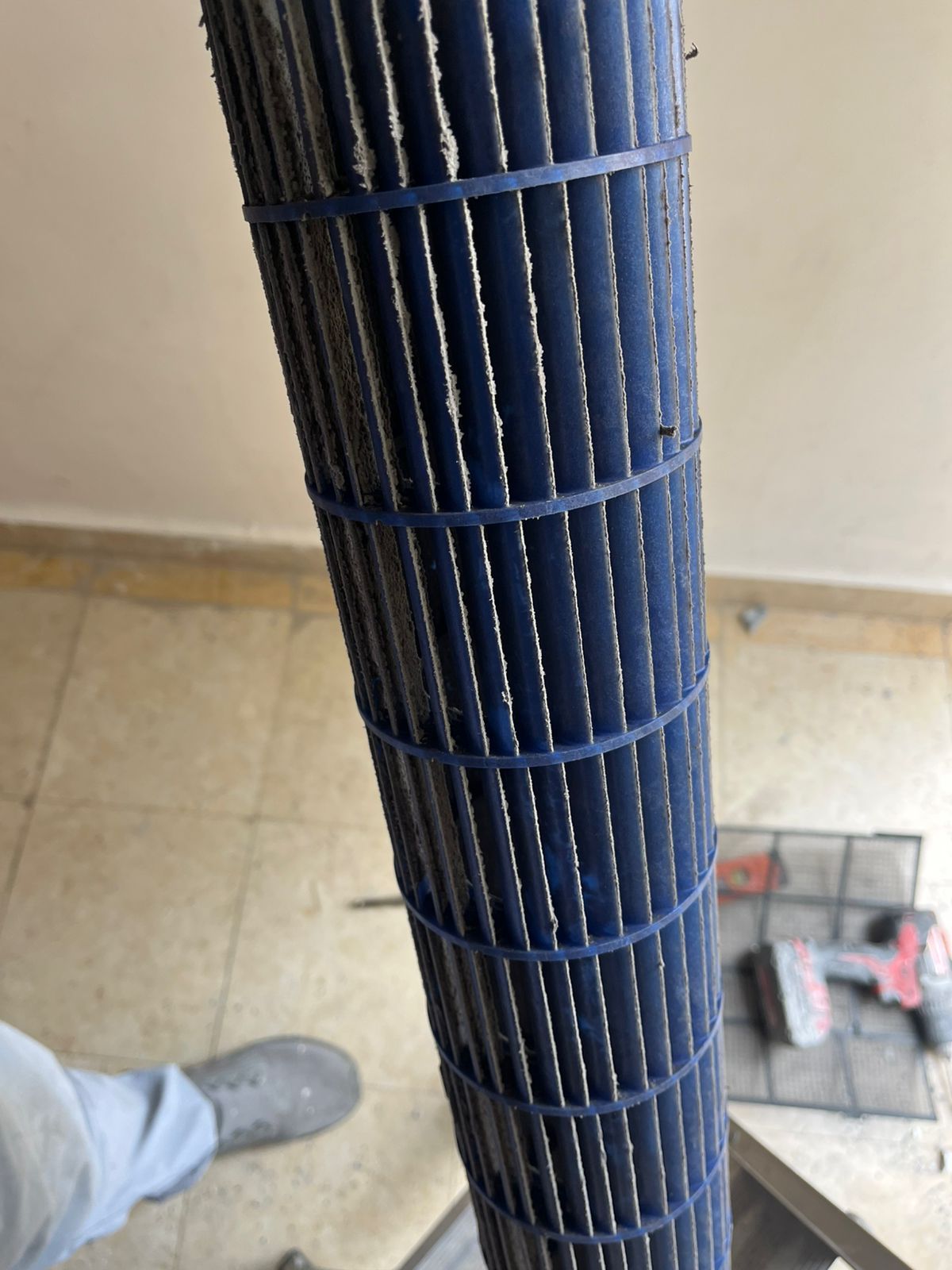 Un primer plano de una rueda del soplador de aire acondicionado de plástico azul oscuro y sucia, sostenida verticalmente sobre un piso de baldosas.