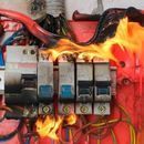 Panel eléctrico en llamas, mostrando cables y disyuntores quemados.