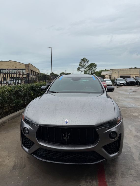 Gray luxury SUV parked in a lot on a cloudy day, front view with raindrops on the hood
