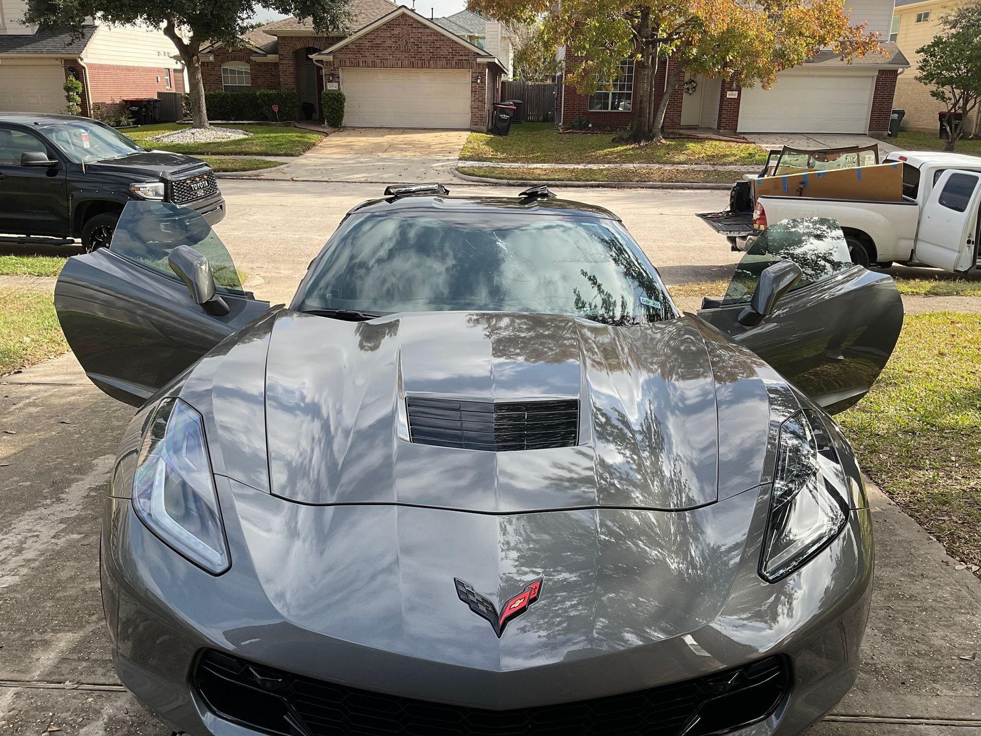 Gray sports car parked on a street with both doors open, front view in a suburban neighborhood.