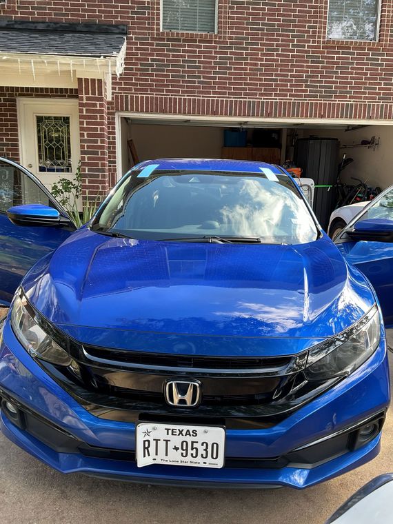 Blue Honda sedan parked in a brick driveway with an open garage behind it