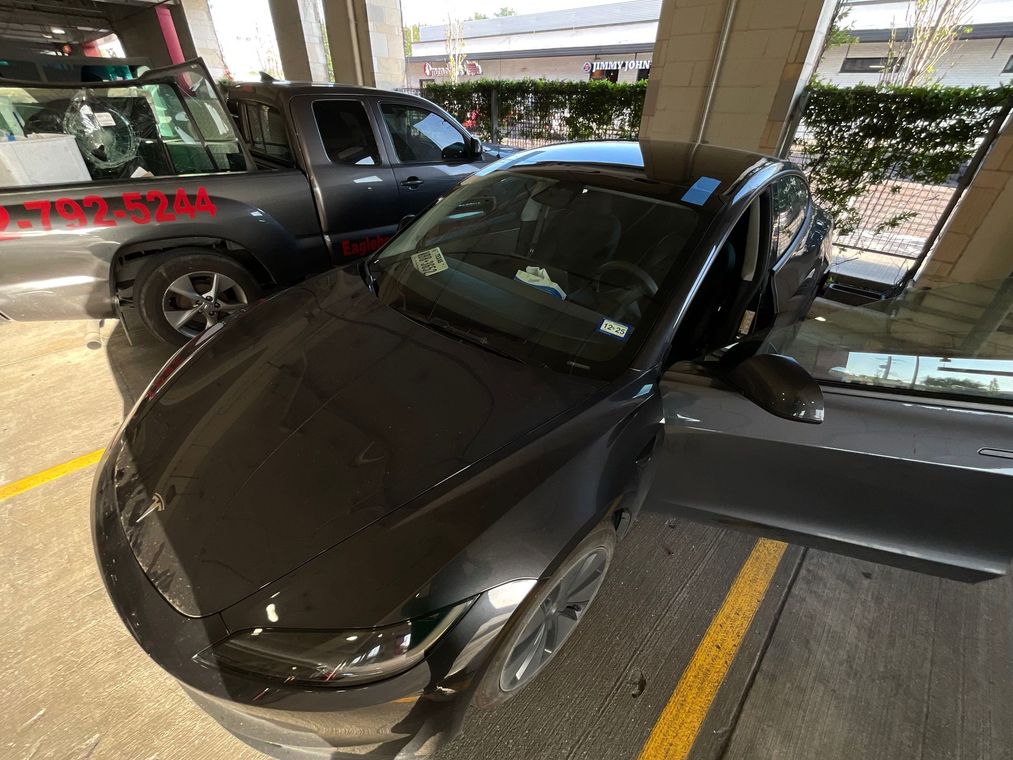 Black sedan parked in a garage, with the driver’s door open beside another vehicle.