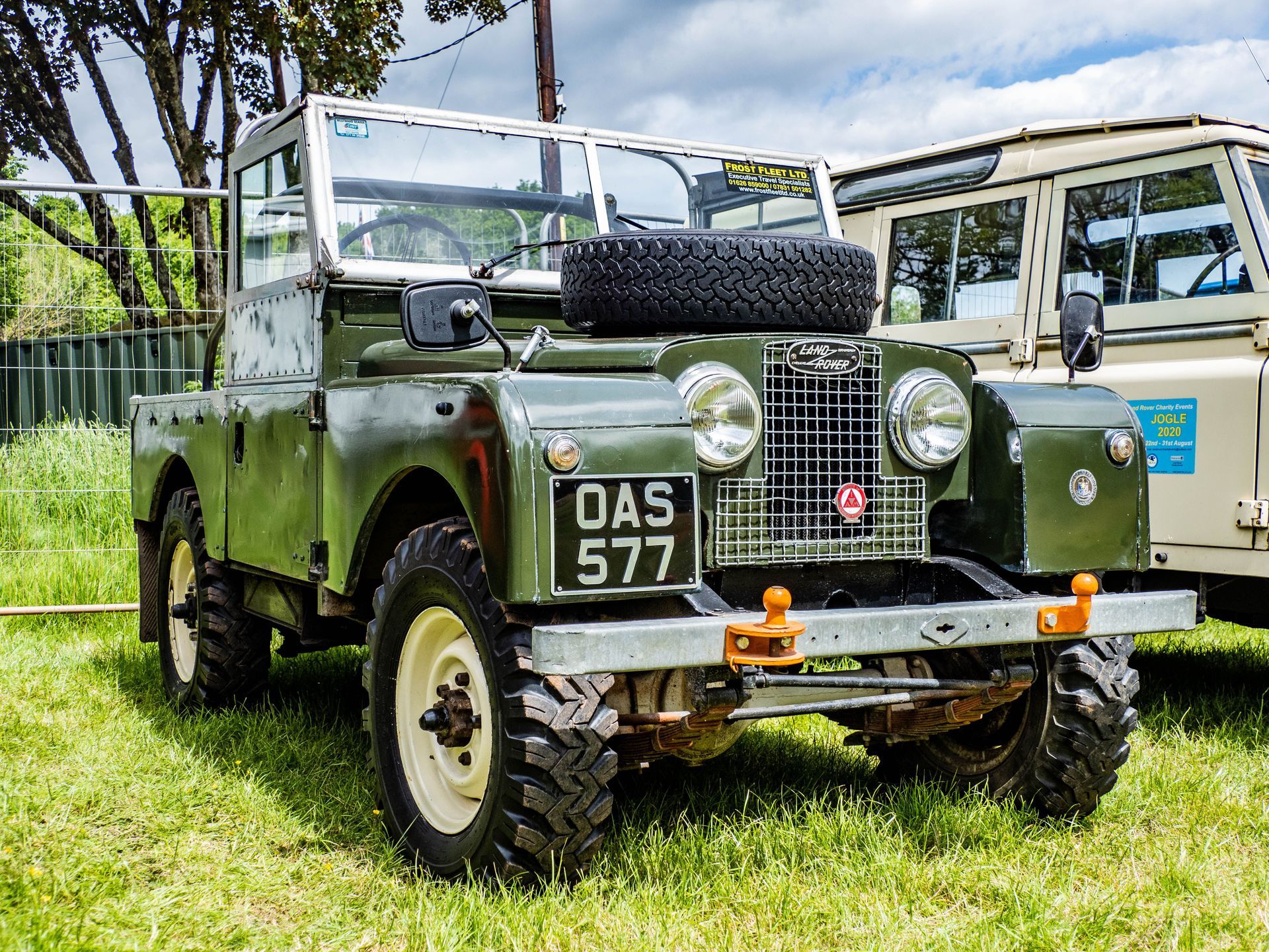 Green vintage off-road jeep parked on grass, with spare tire on the hood and white canvas roof