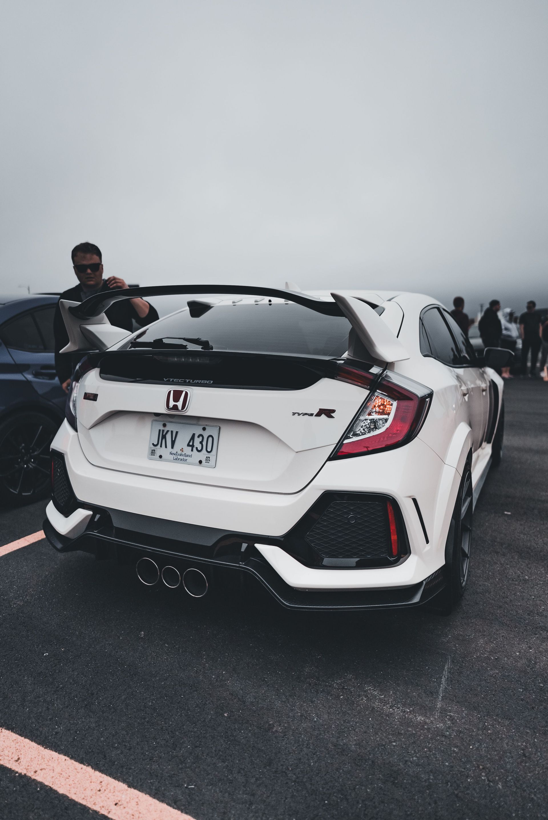 White Honda Civic parked on a wet road with people gathered nearby in foggy weather