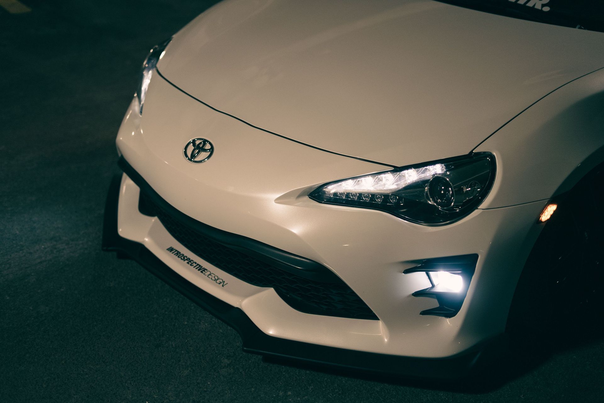 White Toyota sports car front end at night, with headlights on.