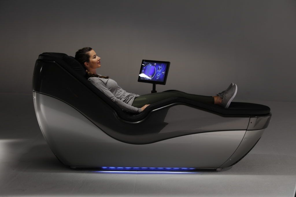 A woman is laying in a hydromassage chair with a monitor on it.