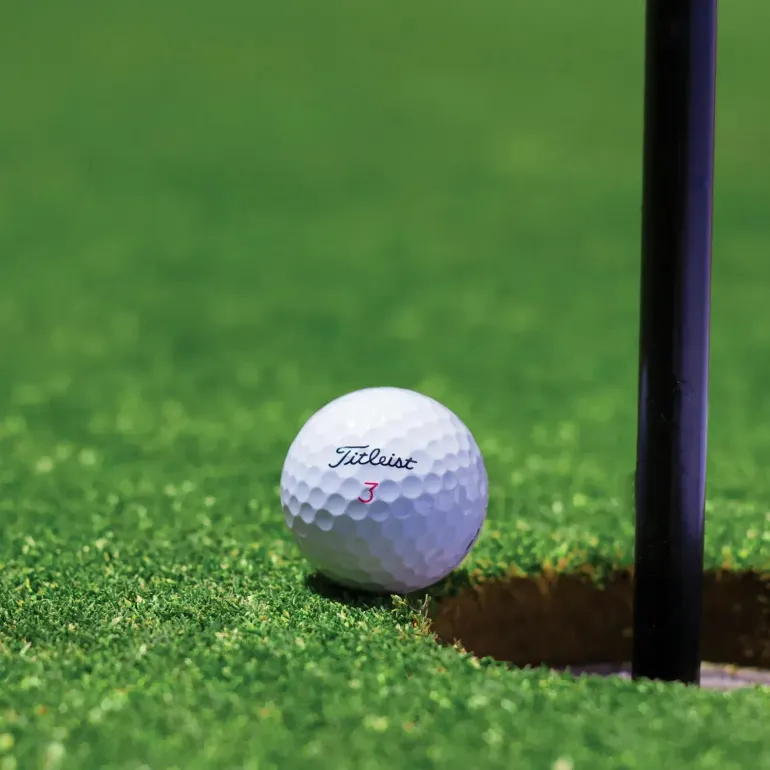 White golf ball beside the hole and flagstick on a green putting surface