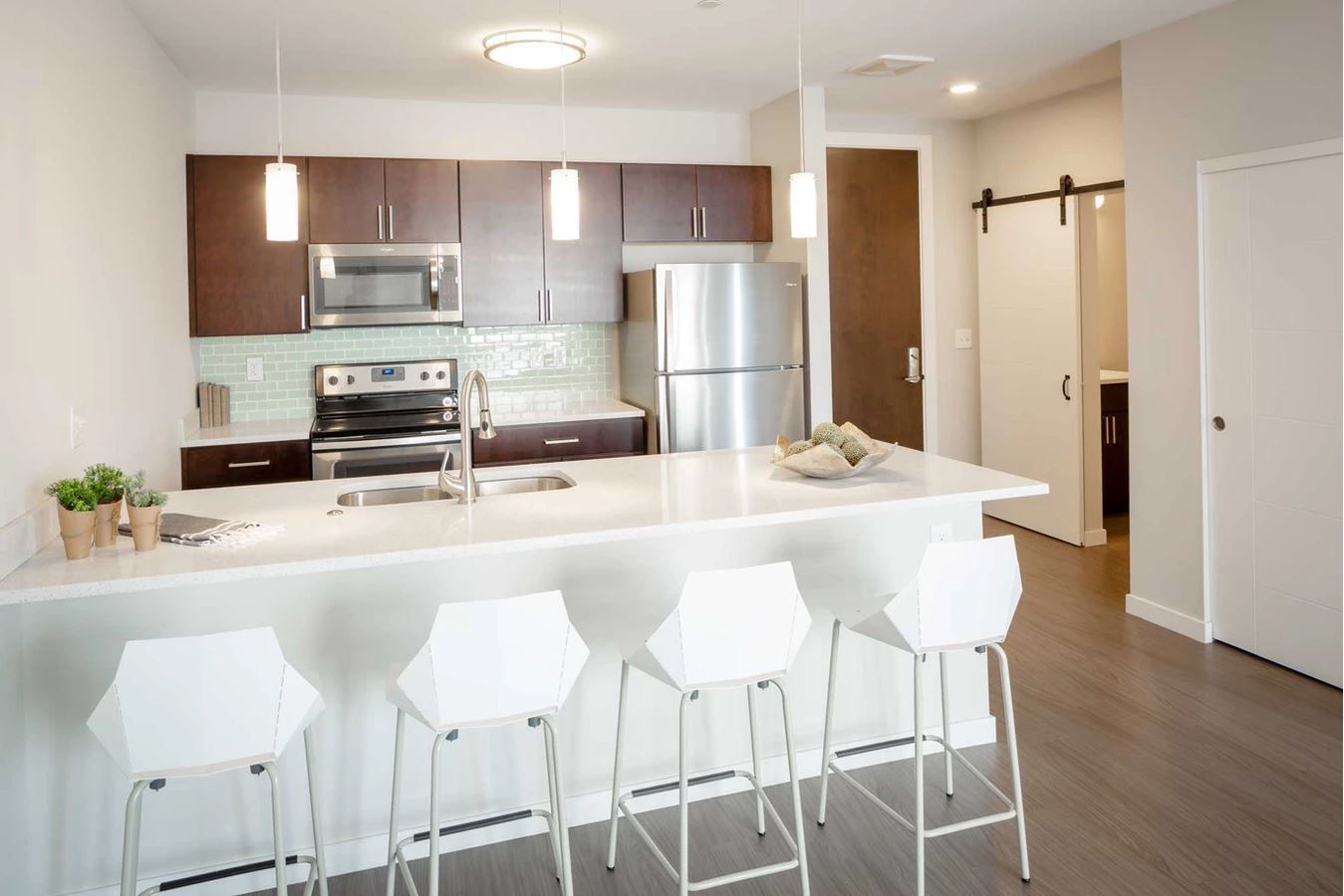 A kitchen with a stove , refrigerator , microwave , sink and bar stools.