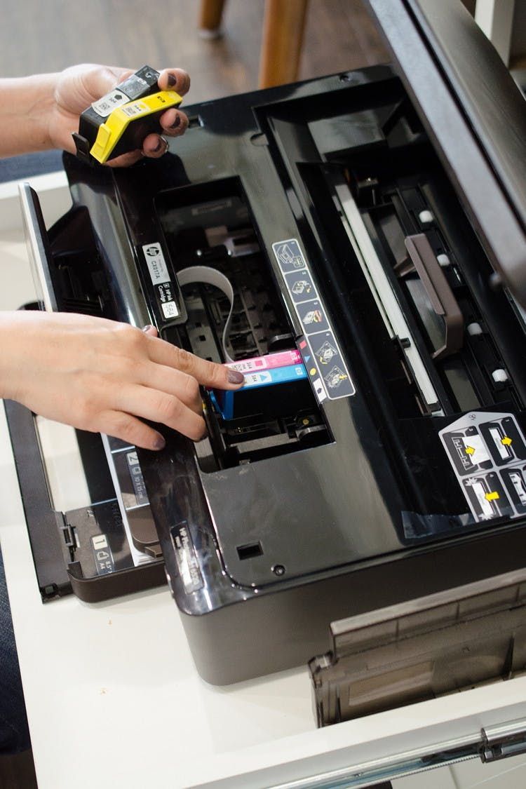 A person is fixing a printer with a yellow tape measure.