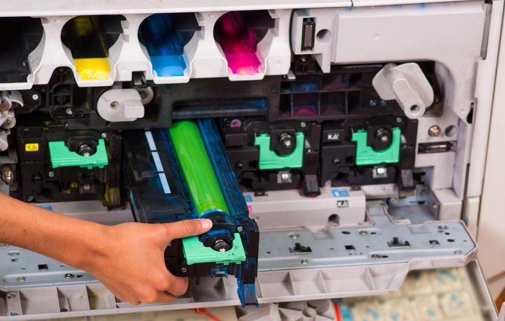 A person is holding a green cartridge in front of a printer.