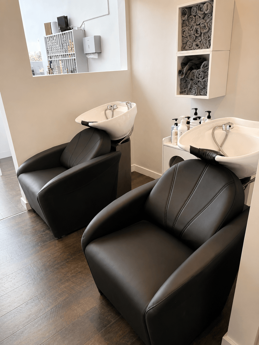 Two black salon chairs with white shampoo sinks in a modern hair washing station.