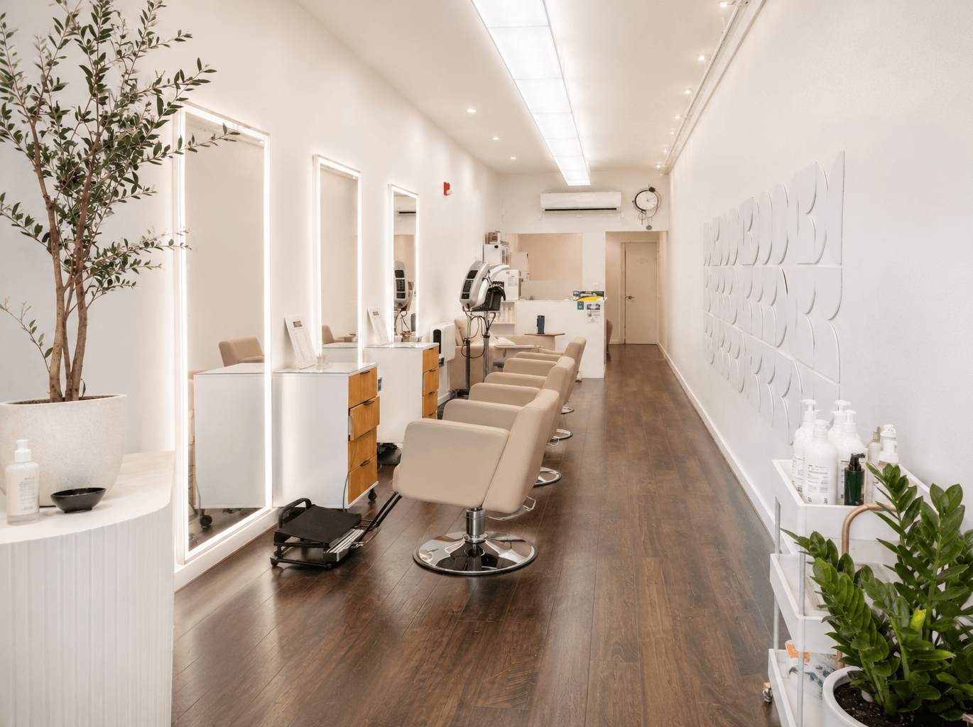 Bright modern hair salon with styling chairs, mirrors, and white decor on dark wood flooring
