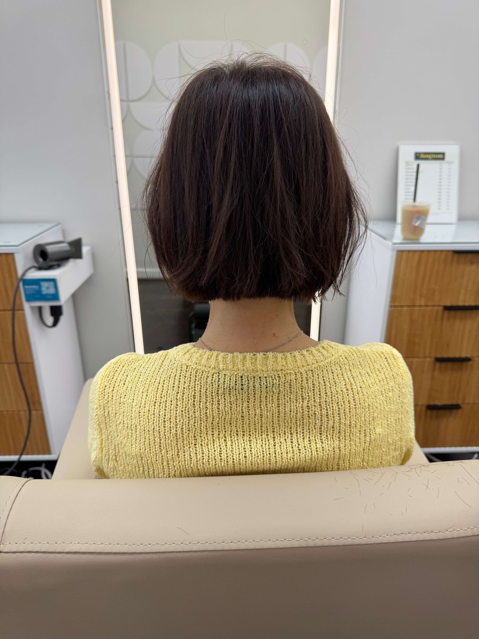 Person with short curly hair seated in a salon chair, viewed from behind.