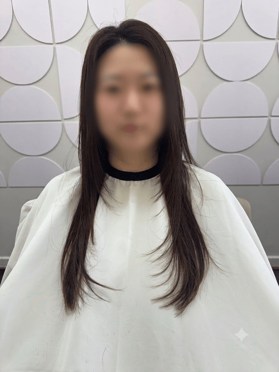 Person with long dark hair wearing a white top, seated against a patterned wall.