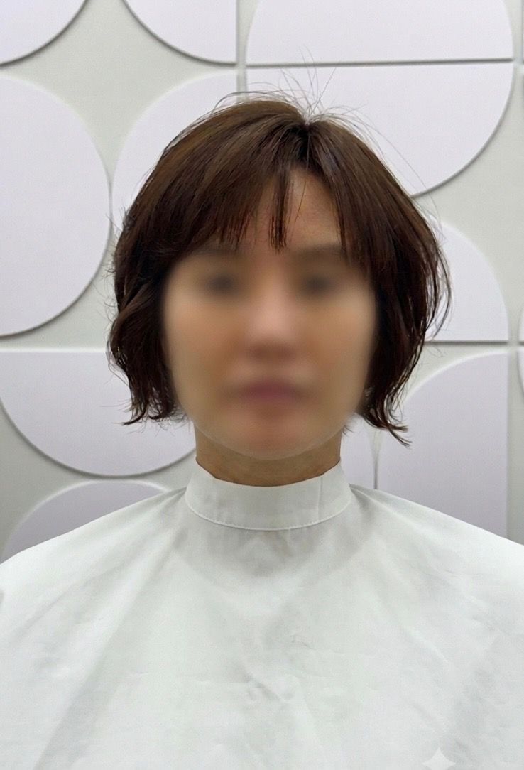 Person with short brown hair in a white salon cape against a light decorative wall.