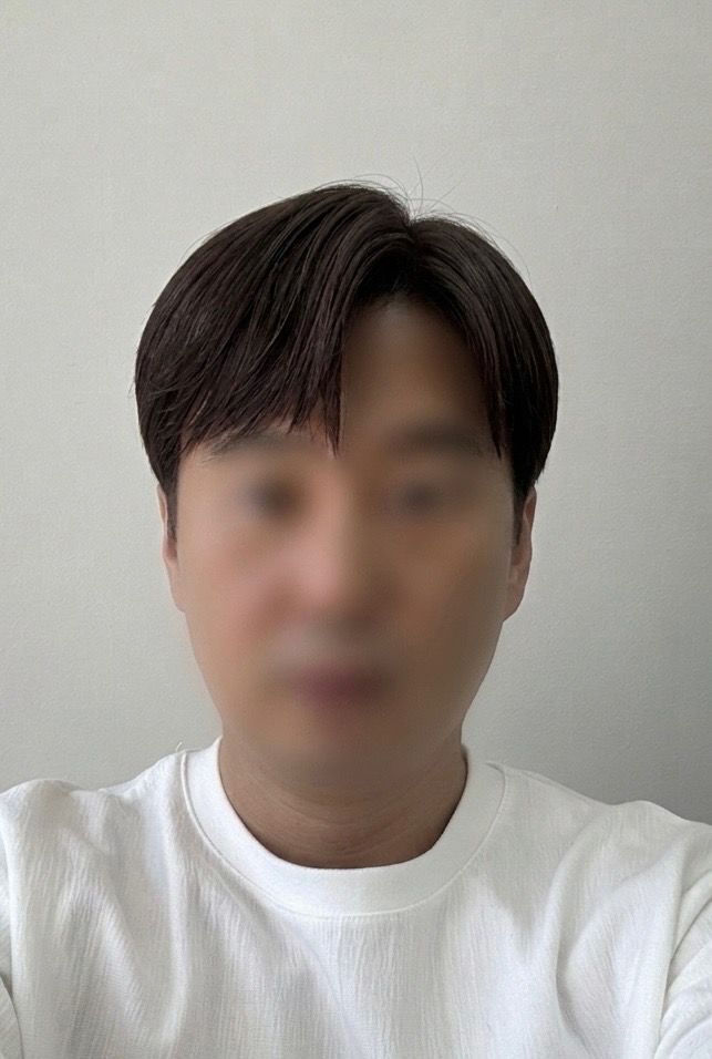 Person in a white shirt taking a selfie against a plain light gray wall.