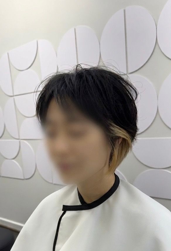 Person with short dark hair in a white salon cape, standing against a wall of white circular panels.