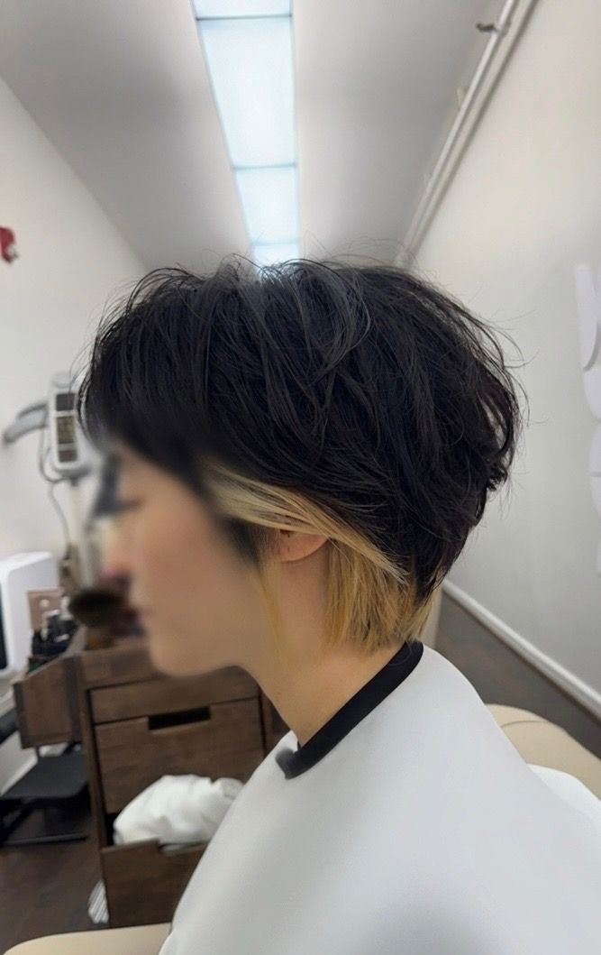 Side profile of a person with short dark hair in a salon chair, wearing a white cape.